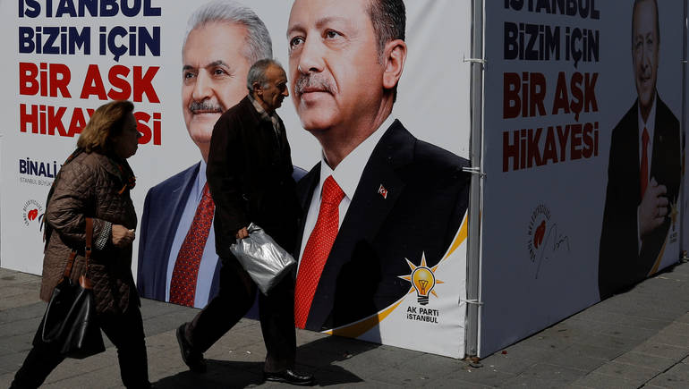 People walk past an AK Party campaign tent with pictures of Turkish President Tayyip Erdogan and his party's candidate for mayor in Istanbul Binali Yildirim for the upcoming local elections in Istanbul